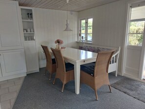 Ein Essbereich mit einem weißen Tisch, Korbstühlen, einem grauen Teppich und einem Fenster mit Blick.