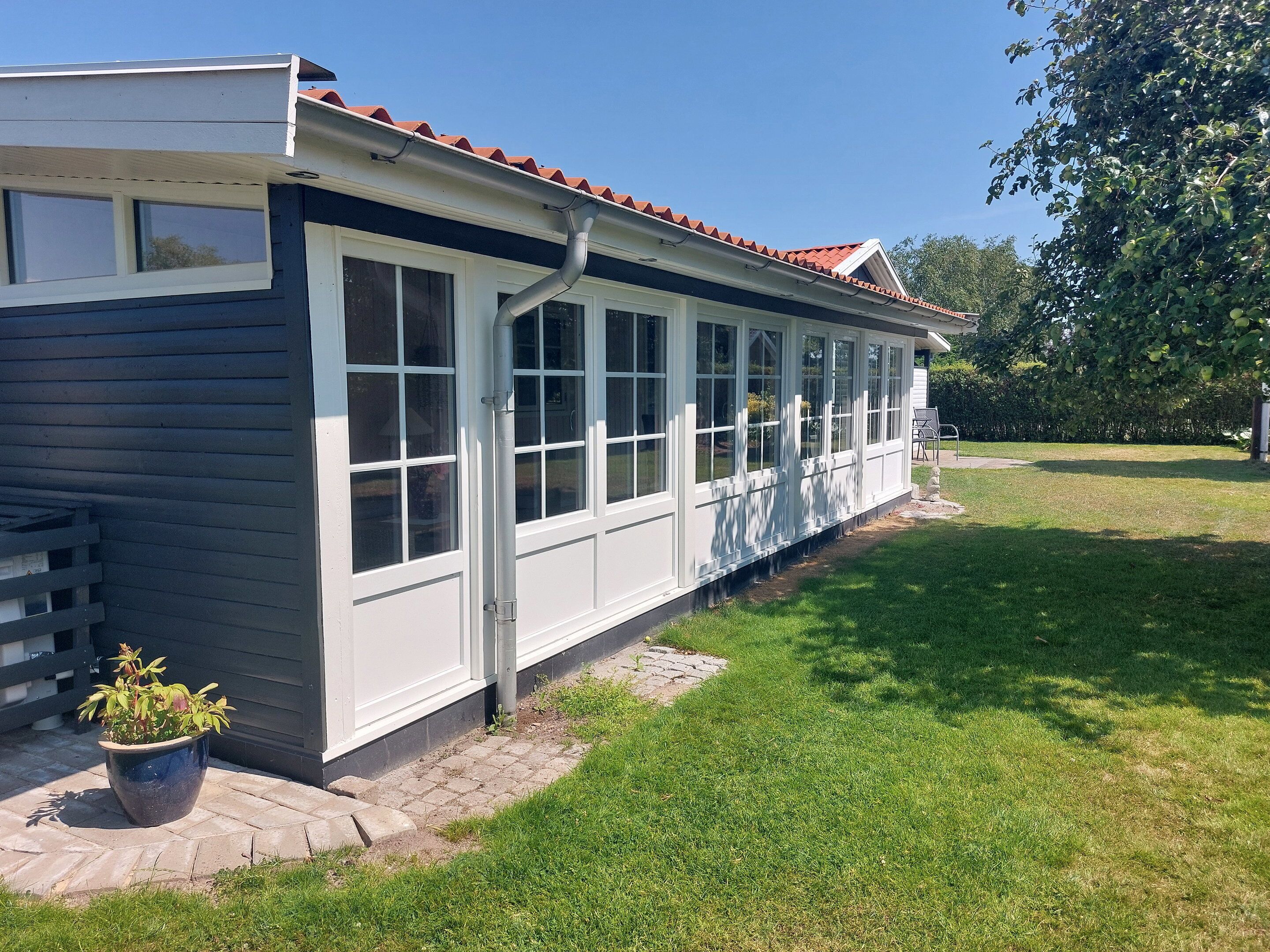 Une maison avec un toit recouvert de tuiles rouges, de grandes fenêtres et une cour verdoyante.