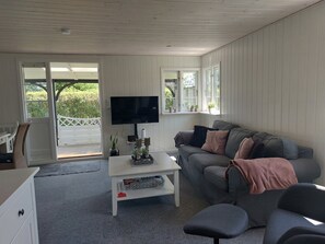 Ein Wohnzimmer mit einer Couch, einem Fernseher, einem Couchtisch und einem Fenster mit Pflanzen.