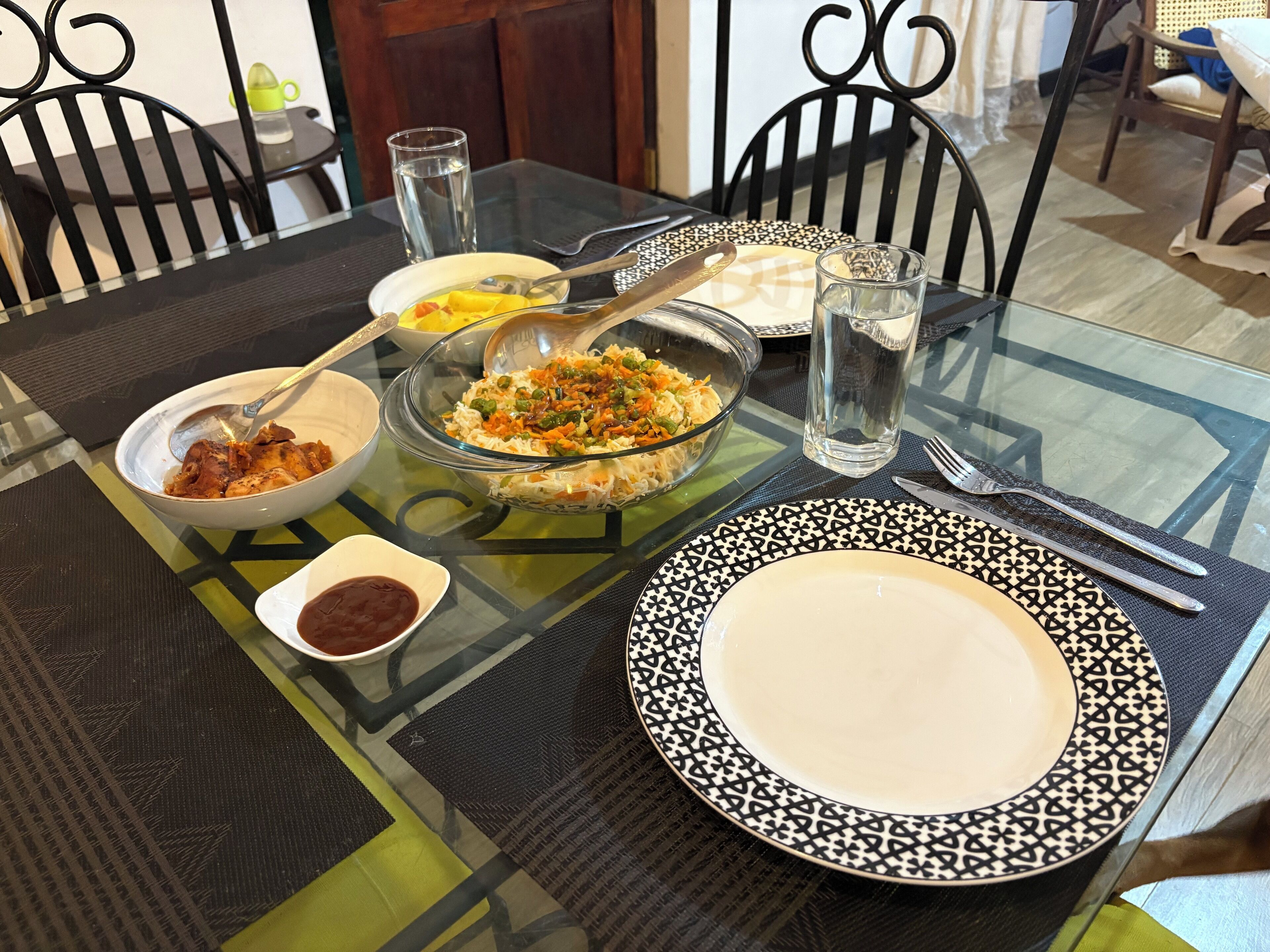 A dining table with various dishes, including a bowl of salad, a bowl of soup, and a plate with a spoon. There are also glasses of water and a small bowl of sauce.