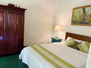Une chambre avec une armoire en bois, une table de chevet avec une lampe, un lit avec une literie verte et blanche, et un tableau représentant un léopard accroché au mur.