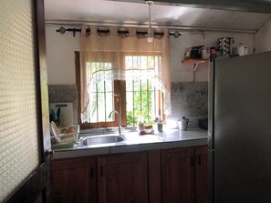 A kitchen with wooden cabinets, a stainless steel sink, and a refrigerator. - Koshi's Lotus room Ella (Bandarawela)