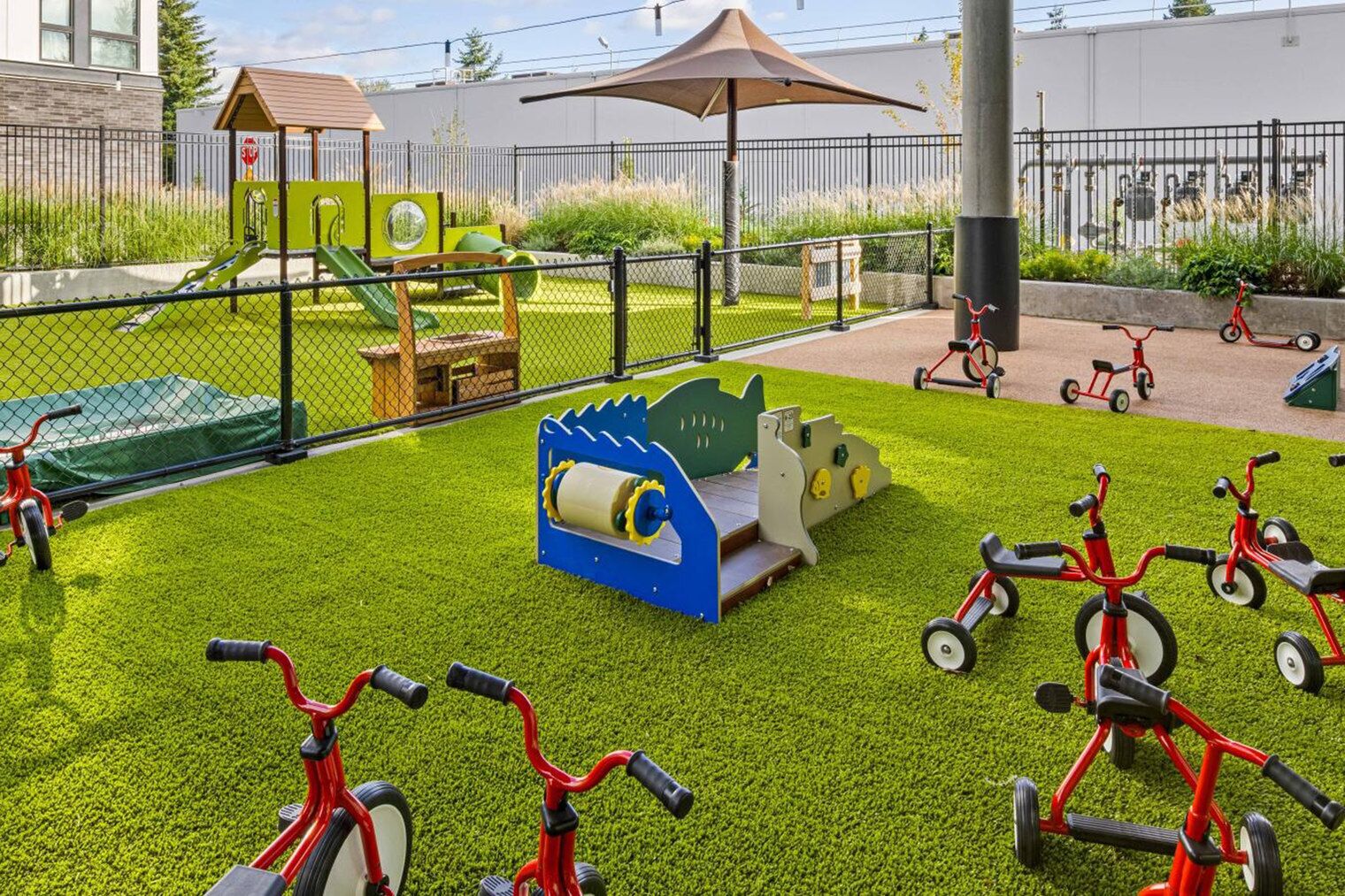 A playground with artificial grass, a playhouse, and red tricycles.