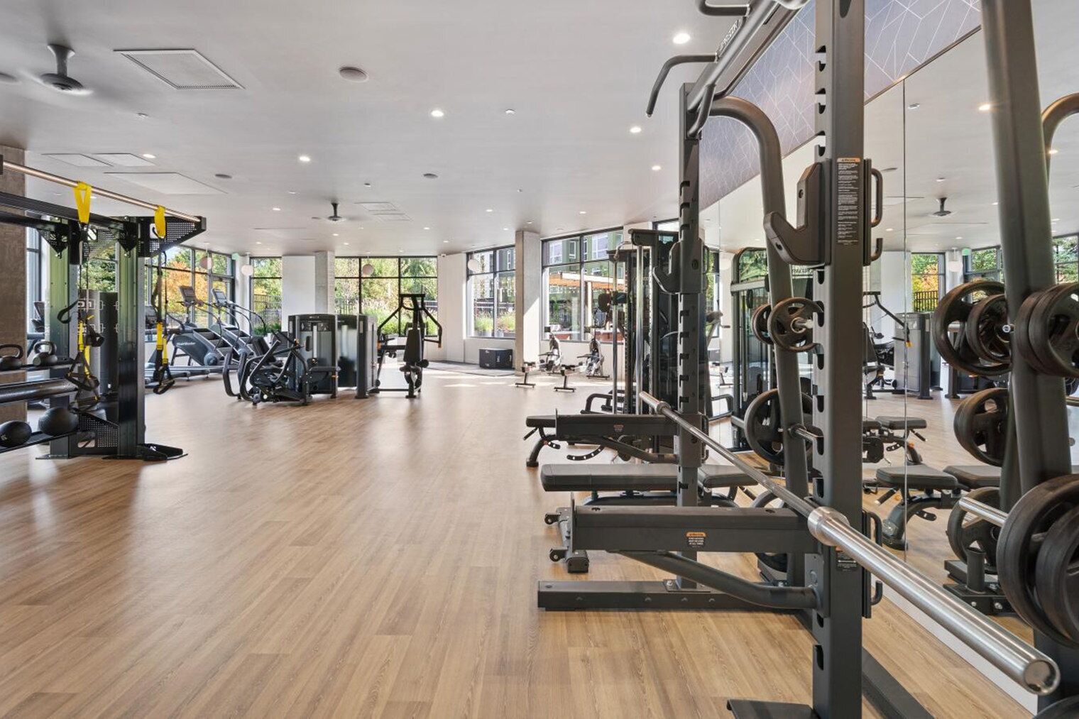 A spacious gym with cardio machines, free weights, and a mirrored wall.