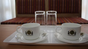 Un plateau avec deux tasses blanches et deux verres transparents, posé sur une table en bois, avec un canapé à rayures en arrière-plan.