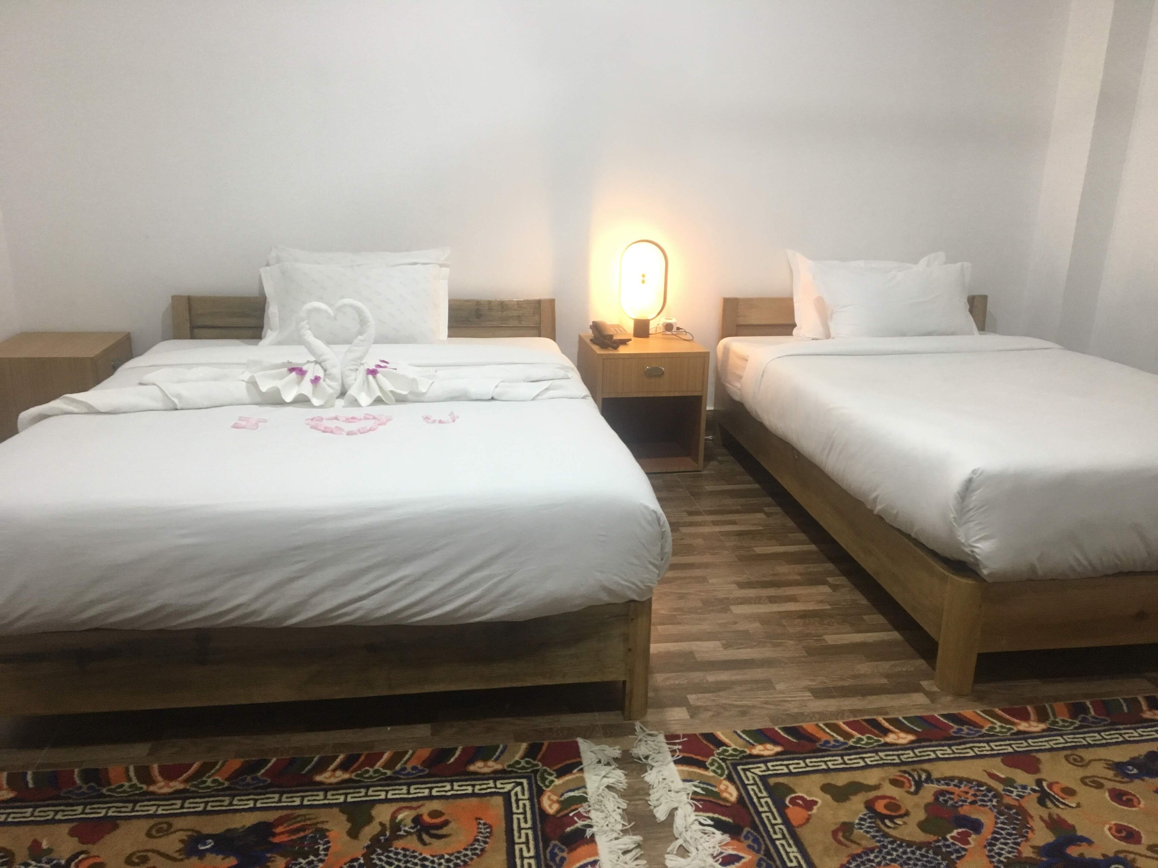 Deux lits simples avec des cadres en bois, du linge de lit blanc et une petite table de chevet avec une lampe.