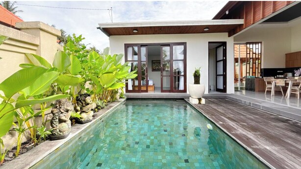 Uma casa moderna com piscina, deck de madeira e um jardim com plantas grandes.