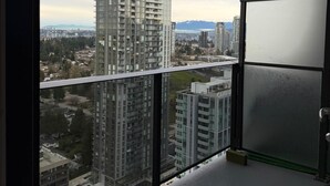 A balcony with a view of high-rise buildings and a distant mountain range. - New 2 Bedroom Home Near Parks + Transit @skytrain &Plaza (Surrey)