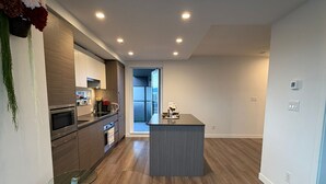 A modern kitchen with wooden cabinets, a central island, and a glass-top table. - New 2 Bedroom Home Near Parks + Transit @skytrain &Plaza (Surrey)