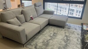 Un soggiorno moderno con un divano angolare grigio, un tappeto soffice grigio e un'ampia finestra con vista sulla città.