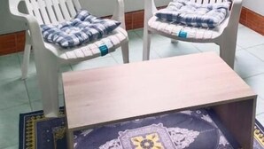 A room with two white plastic chairs with patterned cushions, a small wooden table, and a decorative mat with a central emblem. - Mountain View Hostel - Krabi Airport (Krabi)