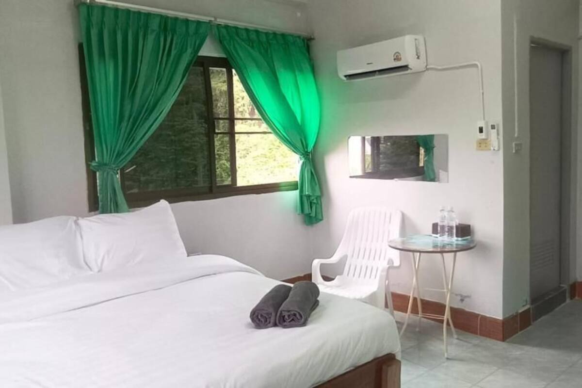 Une chambre d’hôtel avec un lit, une chaise, une petite table, un appareil de climatisation et une fenêtre avec des rideaux.