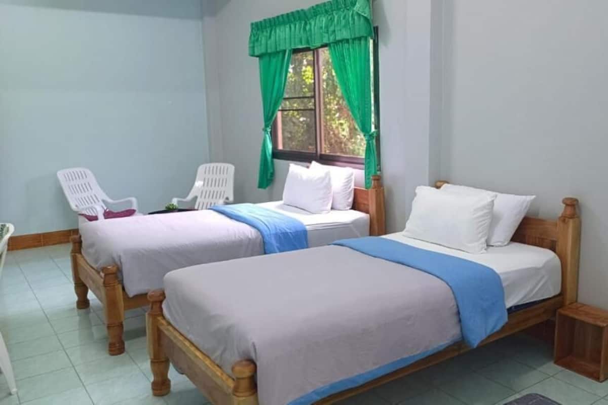 Une chambre avec deux lits simples, une fenêtre avec des rideaux verts et un petit tabouret en bois.