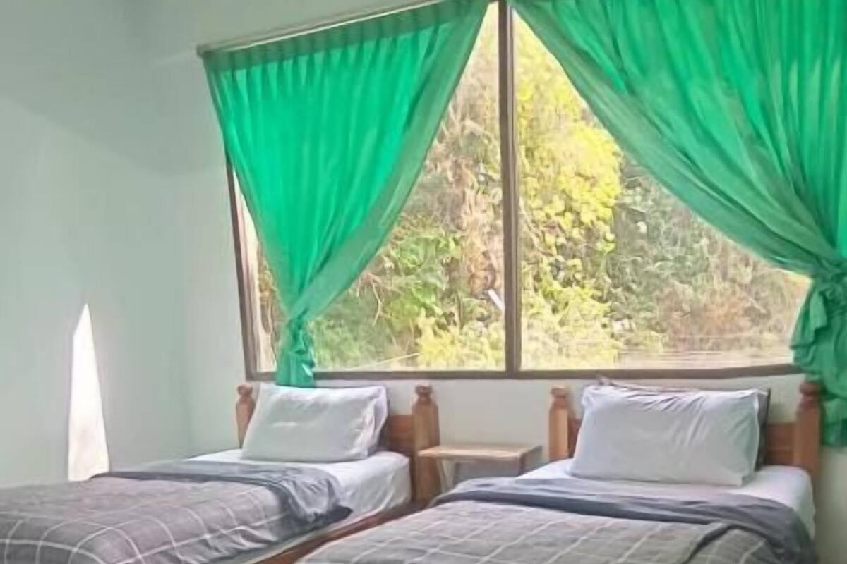 Une chambre avec deux lits, une chaise et une fenêtre avec des rideaux verts.