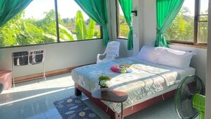 A bedroom with a bed, a chair, a fan, and a view of greenery outside. - Mountain View Hostel - Krabi Airport (Krabi)