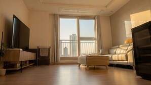 Una sala moderna con una televisión de pantalla plana, un sofá, una mesa de centro y un ventanal con vistas a edificios altos.