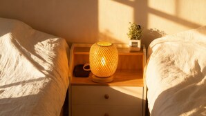 Una cama bien hecha con una mesita de noche que tiene una lámpara, una planta pequeña y un cajón.