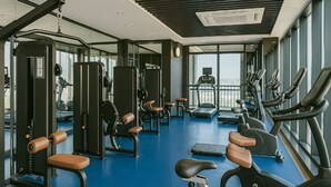 Un gimnasio con diversos equipos de ejercicio, ventanas amplias y vistas a la ciudad.