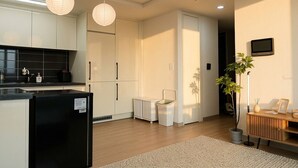 Una cocina moderna con refrigerador, armarios y un lavamanos. Se observa una pequeña silla blanca y una planta en maceta.