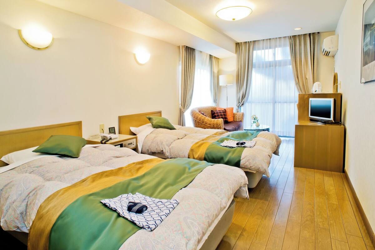 A hotel room with two beds, a chair, a TV, and a desk.