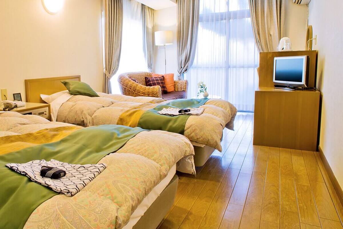 A hotel room with two beds, a television, a chair, and a window with curtains.