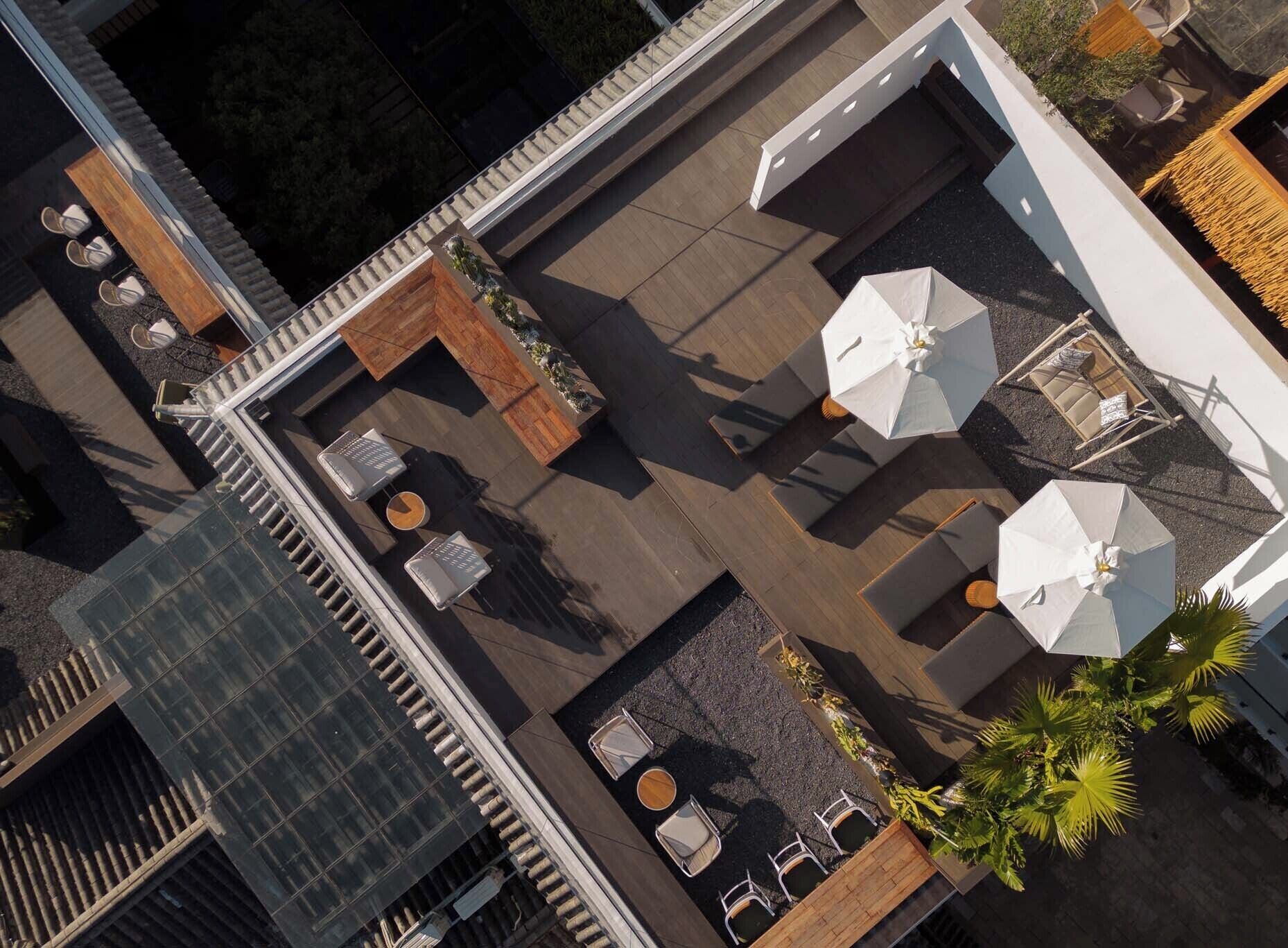 An aerial view of a rooftop patio with outdoor seating, umbrellas, and a small garden area.