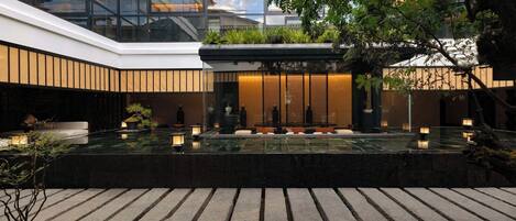 A modern building with a glass facade, a rooftop garden, and a reflective pool with seating.