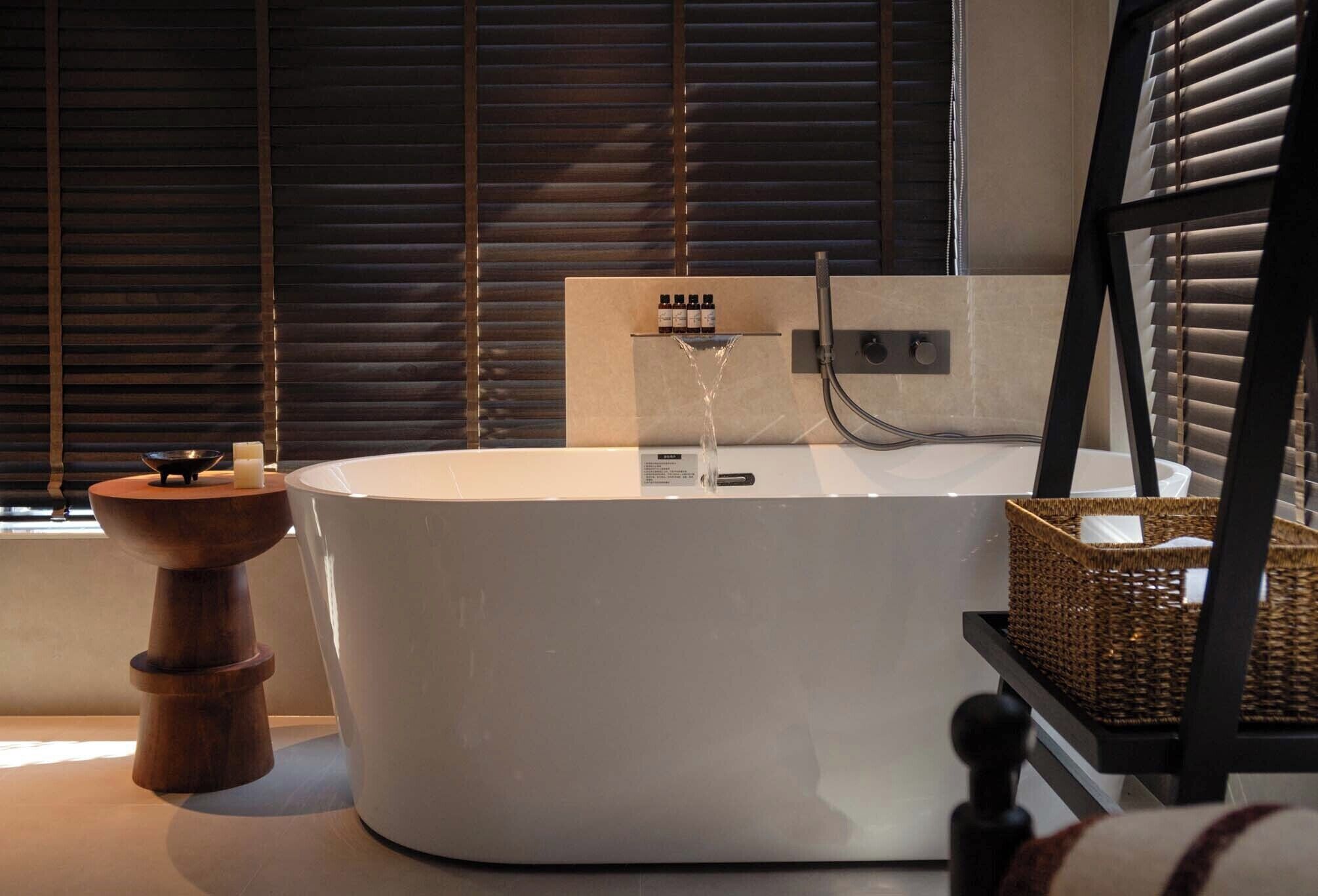 Un baño moderno con una bañera independiente, una mesita de madera y una cesta de mimbre.