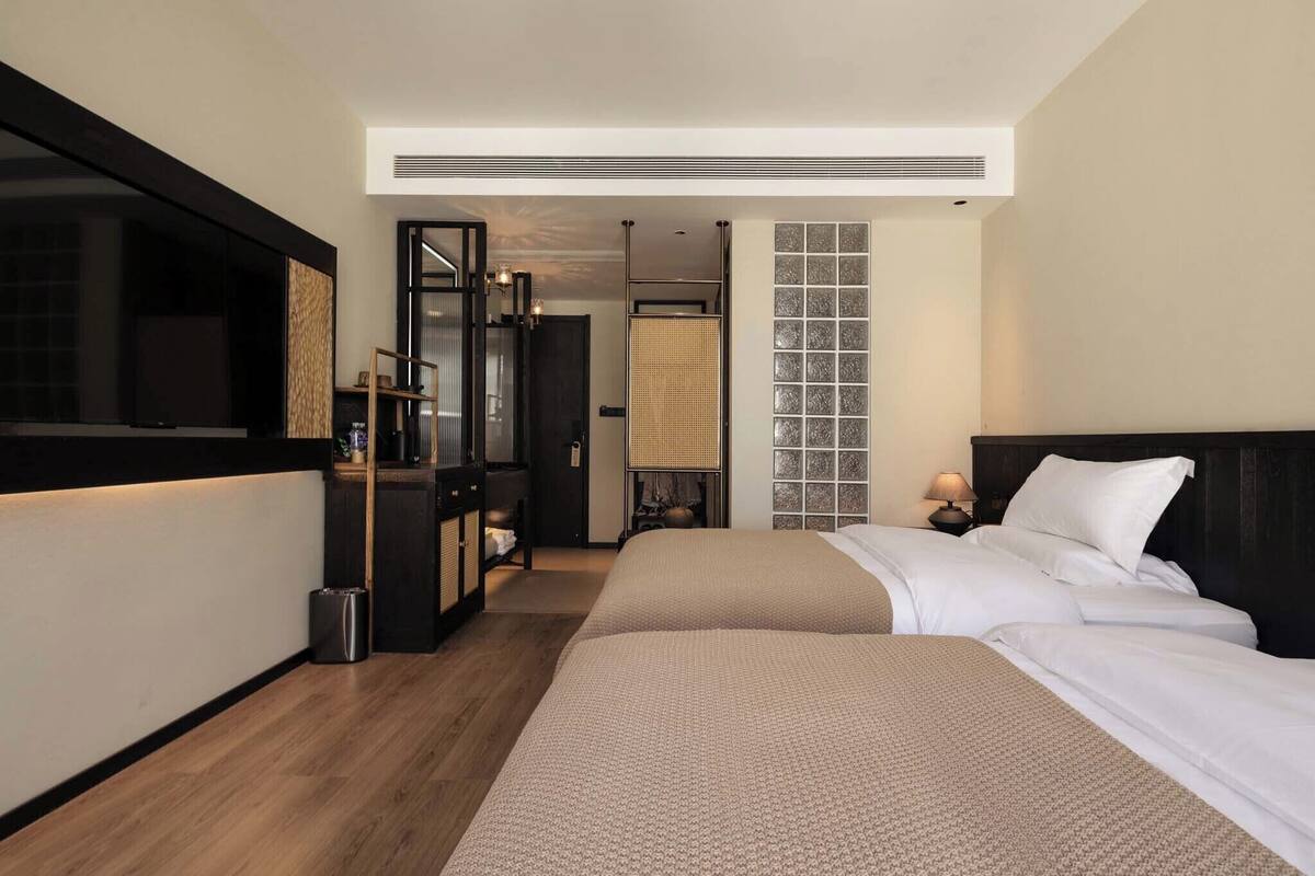 Een hotelkamer met twee bedden, een grote spiegel, een televisietoestel en een kleine tafel met een lamp.