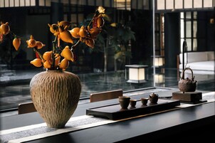 Un conjunto tradicional japonés para la ceremonia del té, con un jarrón de cerámica grande, utensilios para el té y vistas de un edificio a través de una ventana.