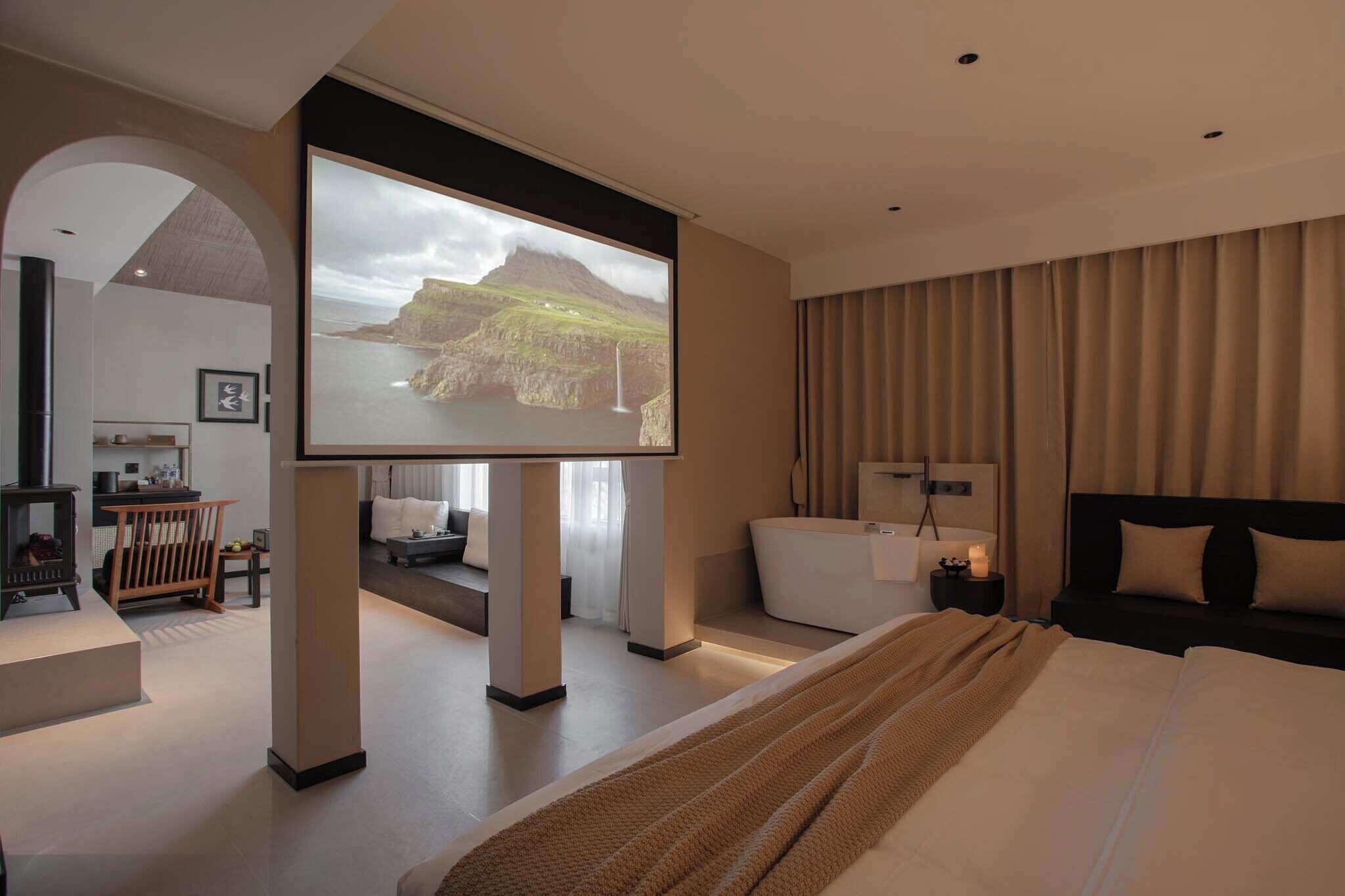 Een moderne hotelkamer met een groot bed, een televisiescherm dat een mooi uitzicht toont, een gezellige zithoek en een aparte badkamer.