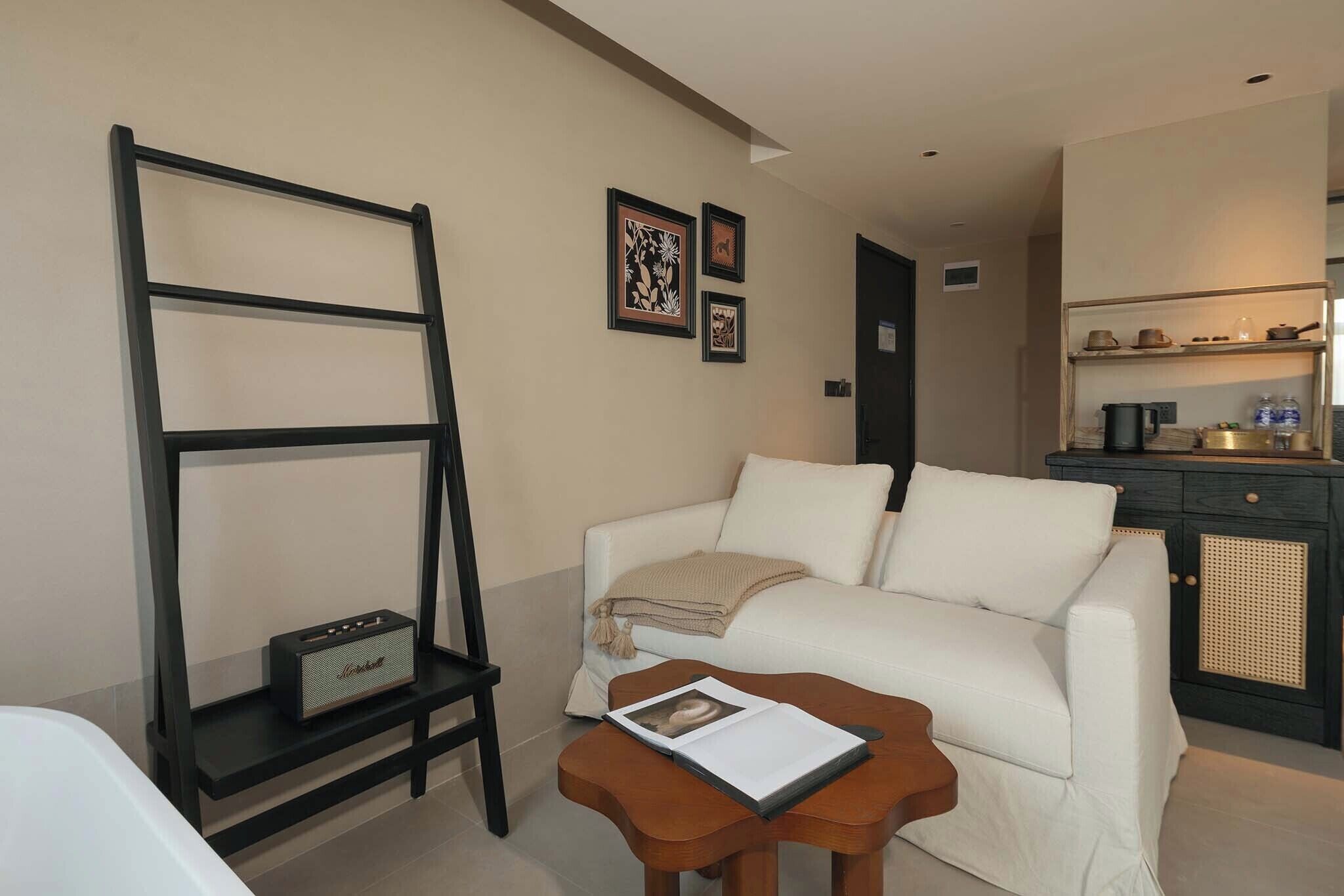 A modern living room with a white sofa, a wooden coffee table, a black shelf unit, and a kitchen area in the background.