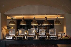 Zona de bar con varias estaciones de preparación de alimentos, iluminación colgante y una selección de bebidas en estantes.