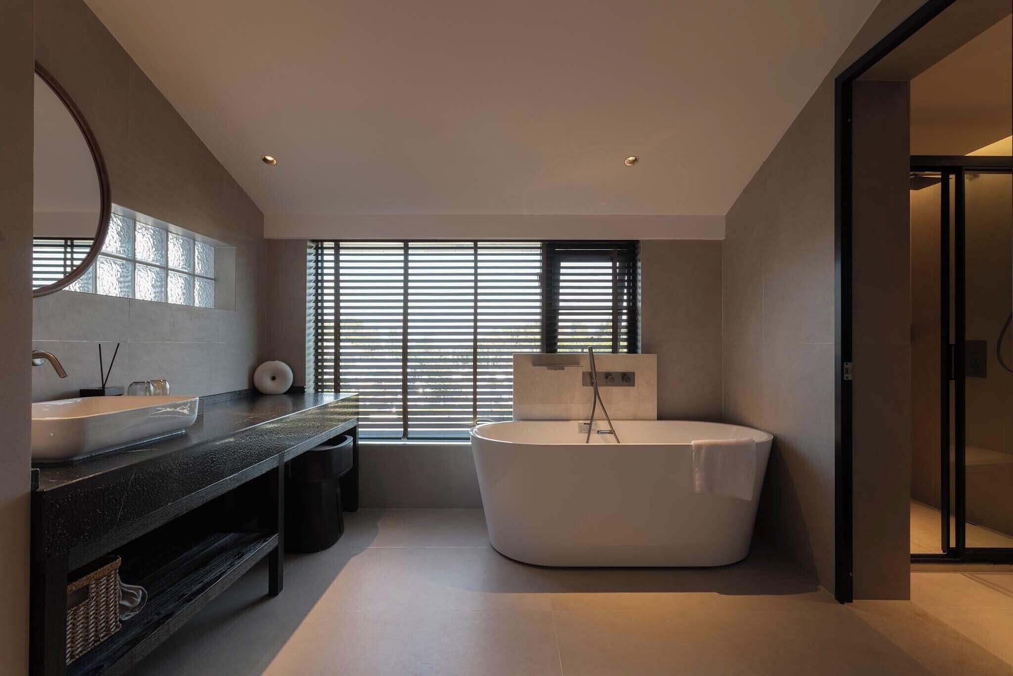 Un baño moderno con una bañera grande, un tocador con espejo y una ventana con persianas.