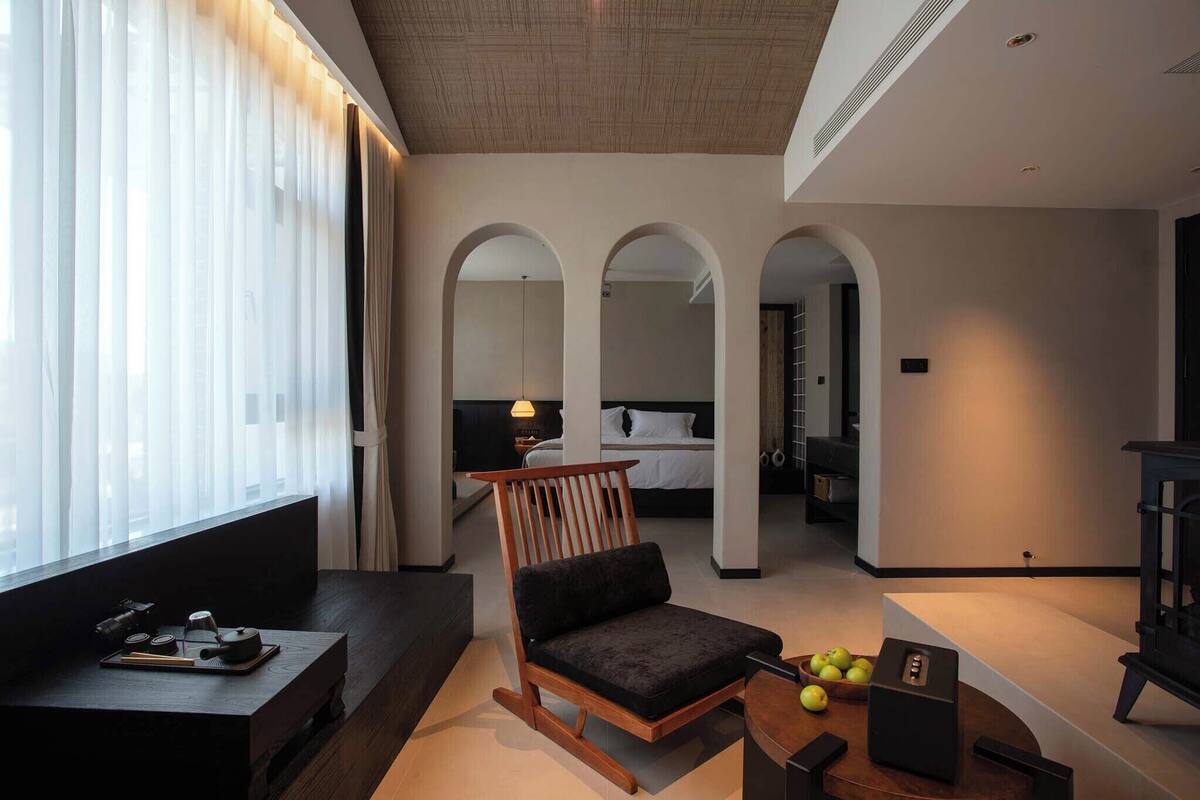 Een hotelkamer met een bed, een houten schommelstoel, een bijzettafeltje met een theepot en een schaal fruit.