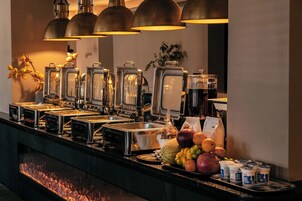 Una mesa de buffet con varios dispensadores de alimentos, una exhibición de frutas y una estación de café.