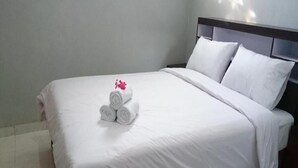 A neatly made bed with white linens and rolled towels, a wooden headboard, and a plain wall. - Hotel Star 88 (Sleman)