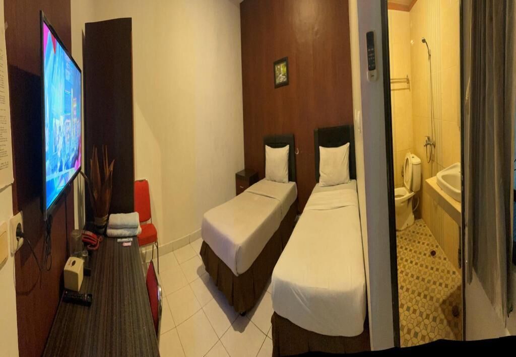 A hotel room with two beds, a TV, a desk, and a shower area.