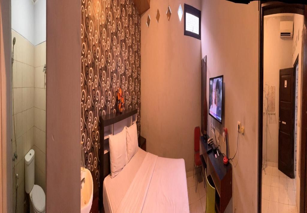 A hotel room with a bed, a bathroom with a toilet and sink, a desk with a computer, and a TV.