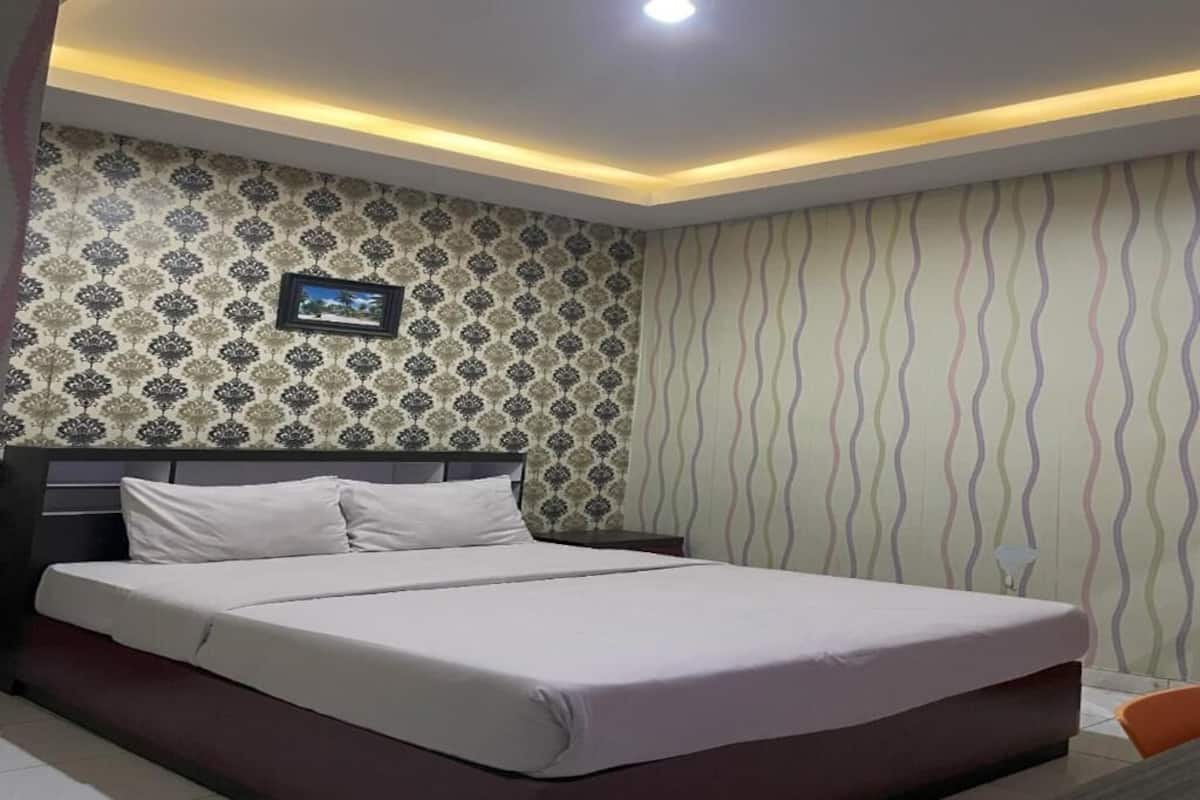 A neatly made bed in a hotel room with patterned wallpaper and a framed picture on the wall.