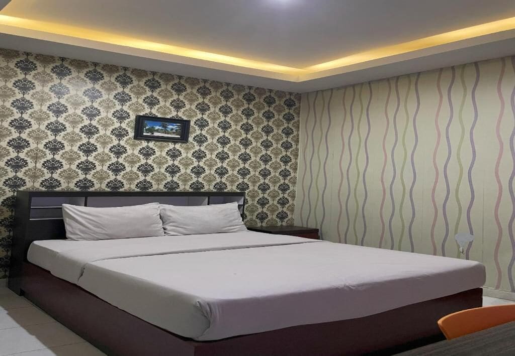 Una cama bien hecha con ropa de cama blanca, un cabecero oscuro y una pared con estampado de papel tapiz.
