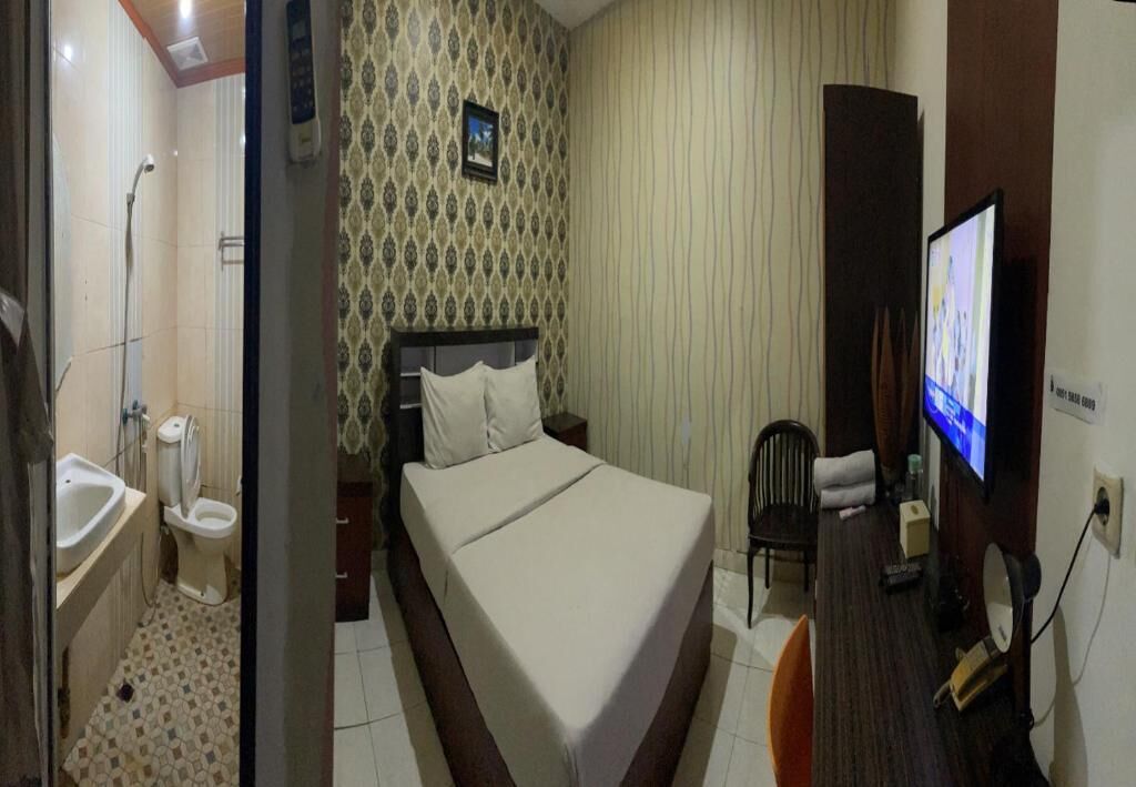 Hotelkamer met een bed, een televisie, een bureau, een stoel, een badkamer met wastafel en toilet, en een behangen wand.