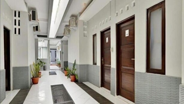 A hallway with a tiled floor, potted plants, and wooden doors. - Hotel Star 88 (Sleman)