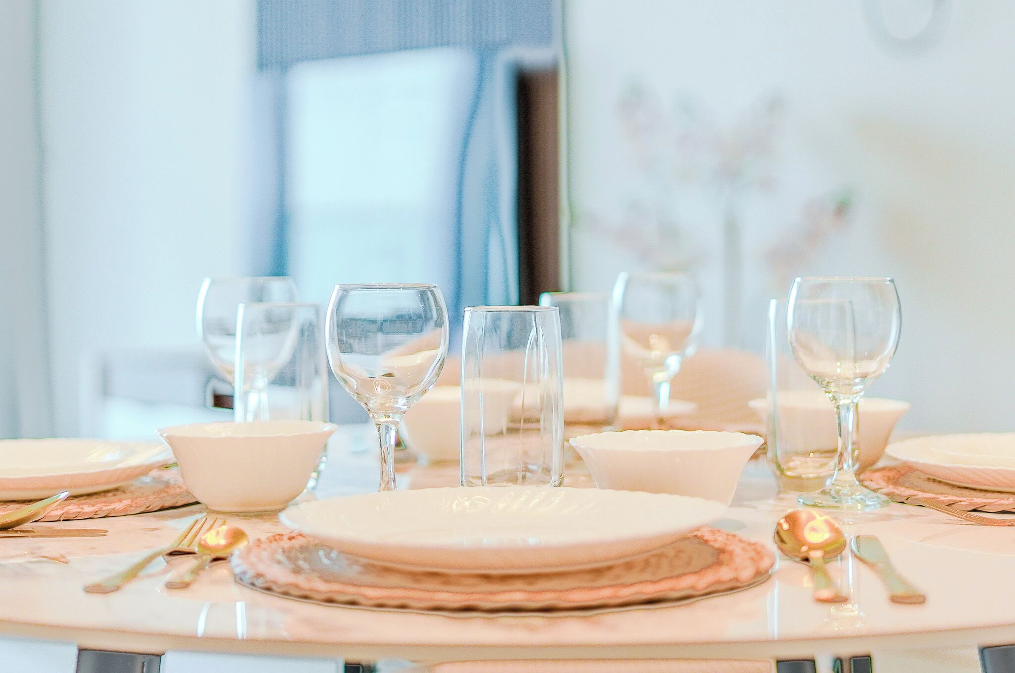 Una mesa redonda dispuesta con platos blancos, cuencos y copas de cristal.