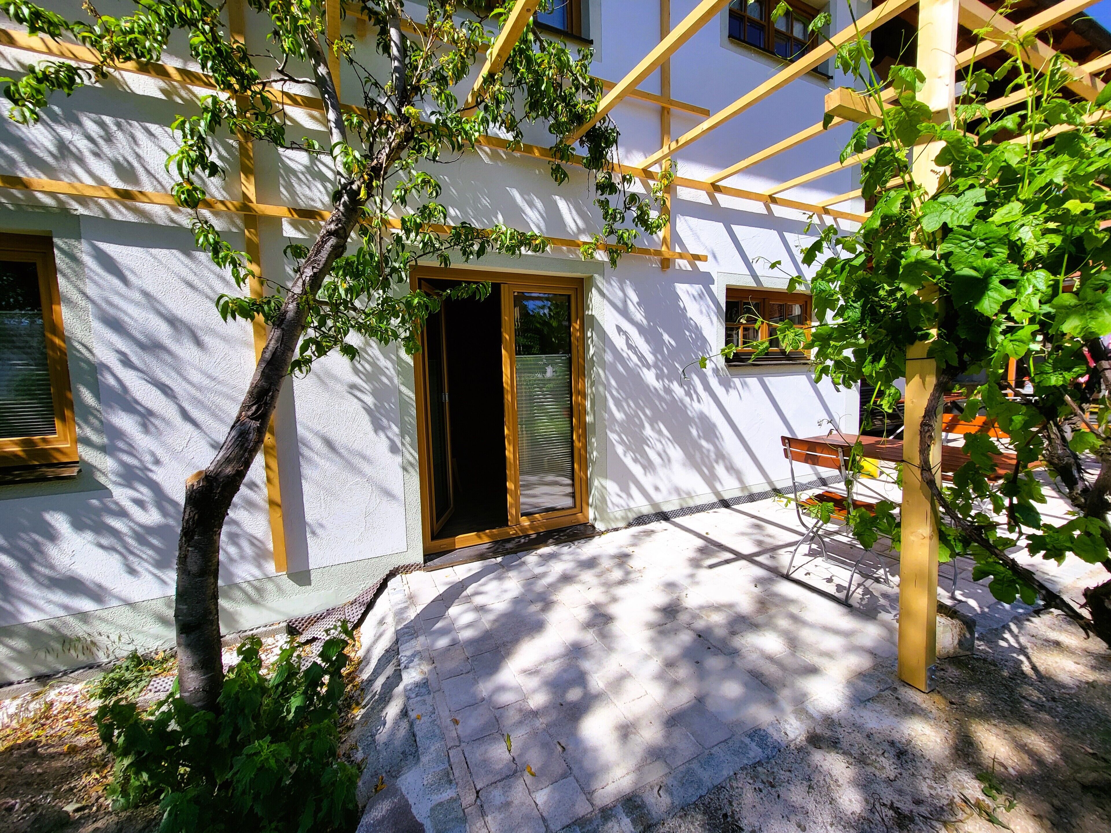 En bygning med hvide facader, en træpergola og en dør ind til et rum.