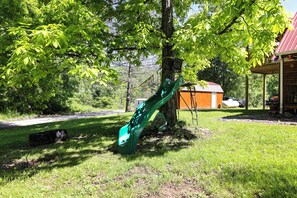 A playground with a slide, a tree, and a building with a red roof. - Family Cabin! Close to Greenbrier River & Snowshoe (Cass)