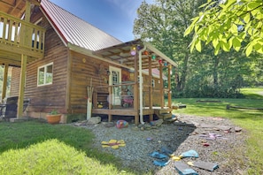 A wooden cabin with a porch, a small deck, and a garden area with rocks and a flower bed. - Family Cabin! Close to Greenbrier River & Snowshoe (Cass)