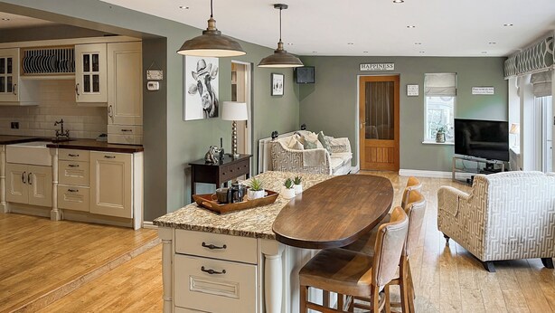 A modern kitchen with a central island, bar stools, and a dining area with a television. - 4 bedroom accommodation in Bishop Auckland (Bishop Auckland)