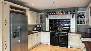 A modern kitchen with white cabinetry, a stainless steel refrigerator, a black stove, and a wine rack above the counter. - 4 bedroom accommodation in Bishop Auckland (Bishop Auckland)
