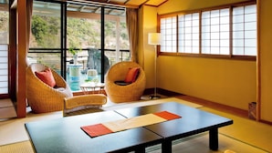 Una habitación japonesa tradicional con suelo de tatami, una mesa baja, dos sillas de mimbre y un amplio ventanal con paneles shoji.